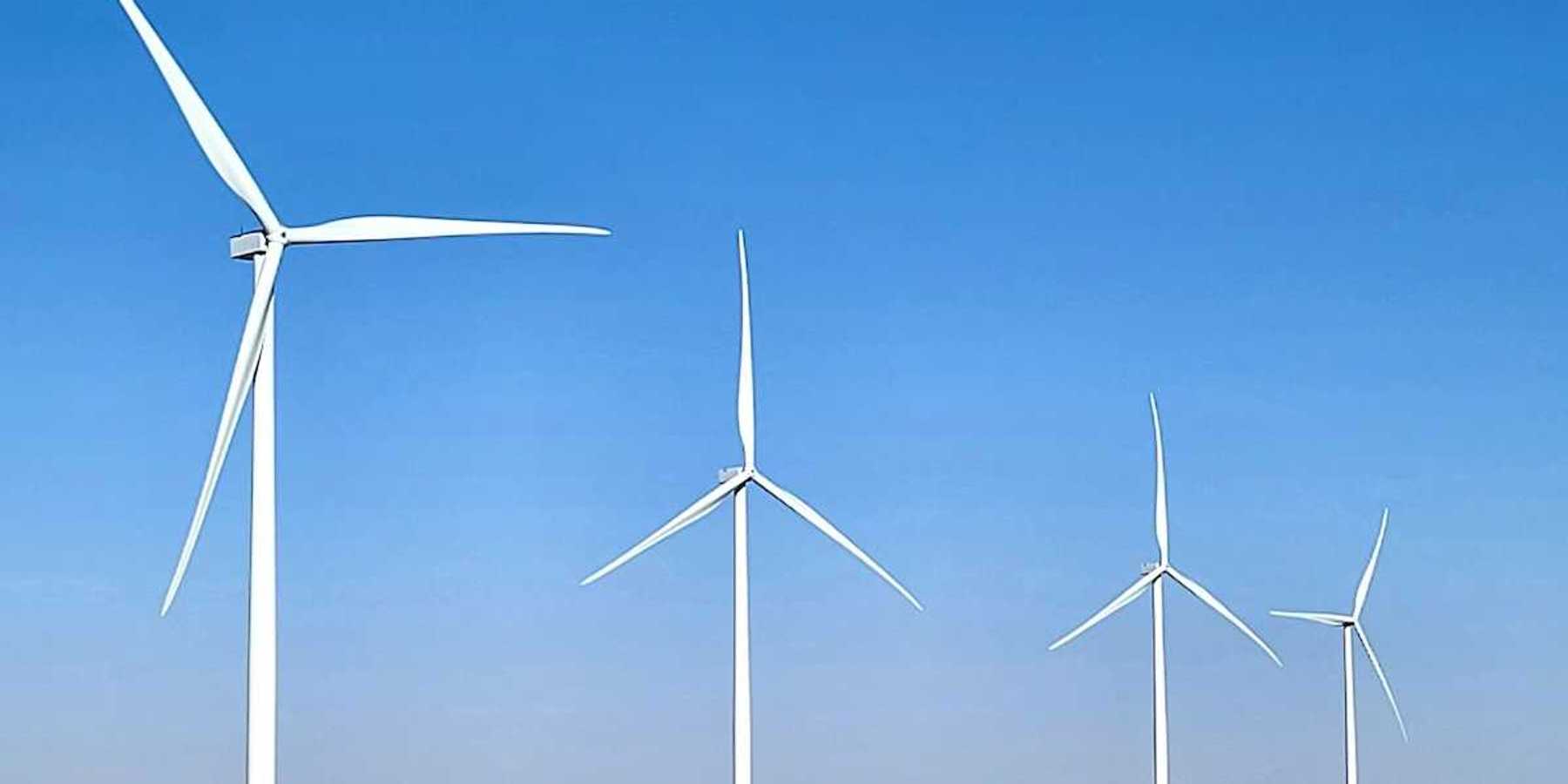 Four wind turbines in a row standing in a flat brown field.