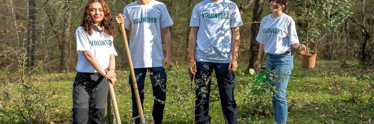 Four young people wearing t-shirts that read "volunteers" equipped to plant trees.
