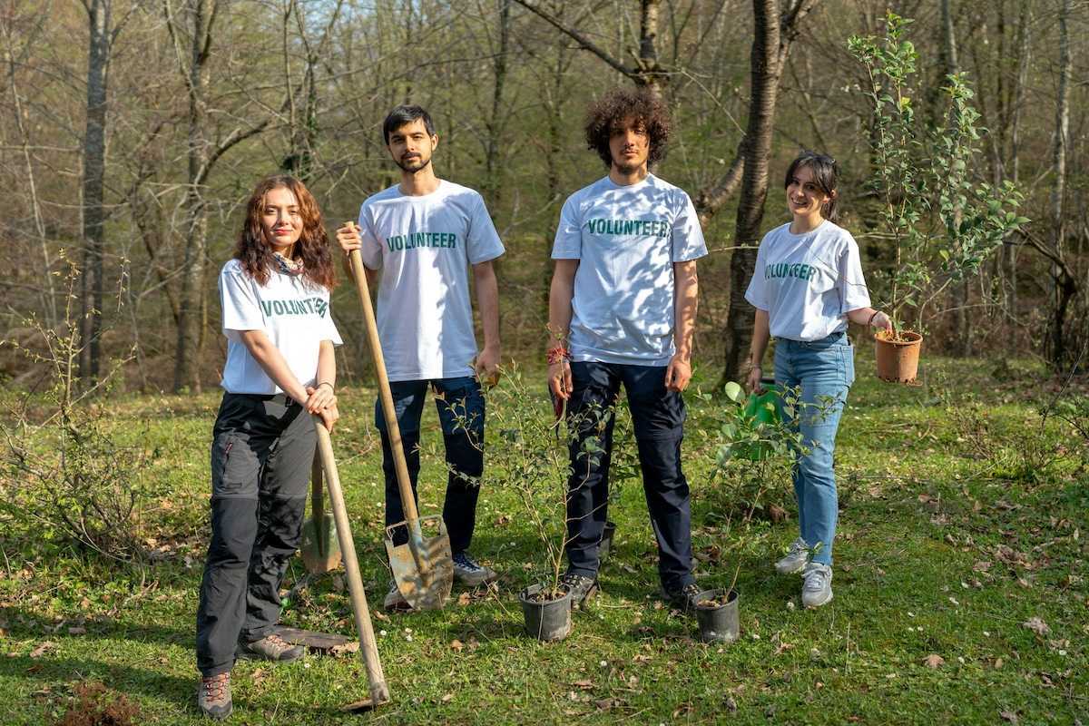 Four young people wearing t-shirts that read "volunteers" equipped to plant trees.