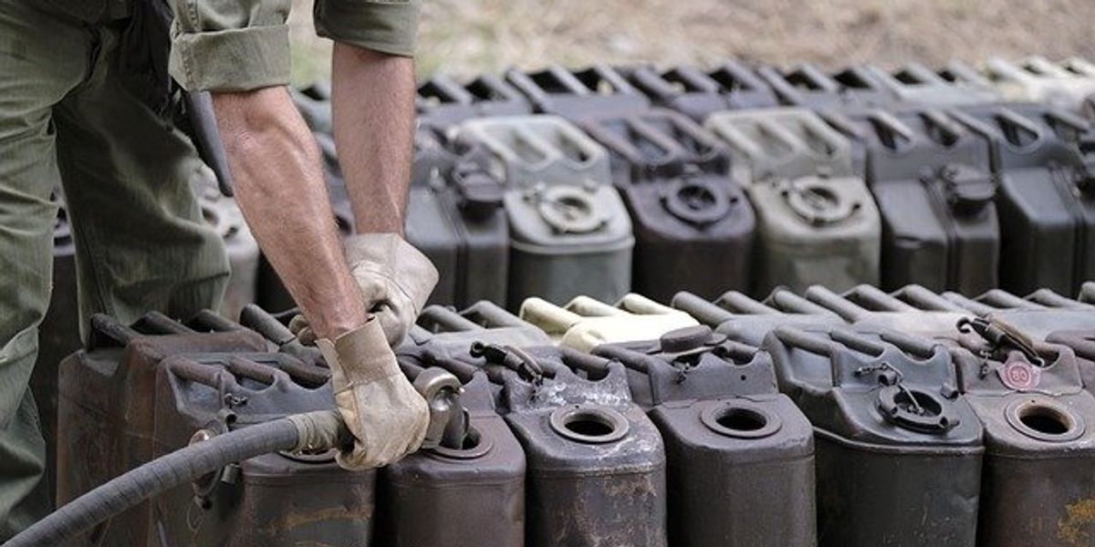 Gas cans being filled by a person wearing green clothing.