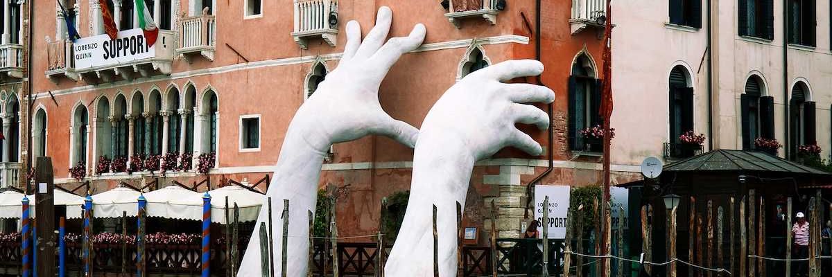 Gigantic hands rise from water to support the Ca' Sagredo Hotel, a statement of the impact of climate change and rising sea levels.