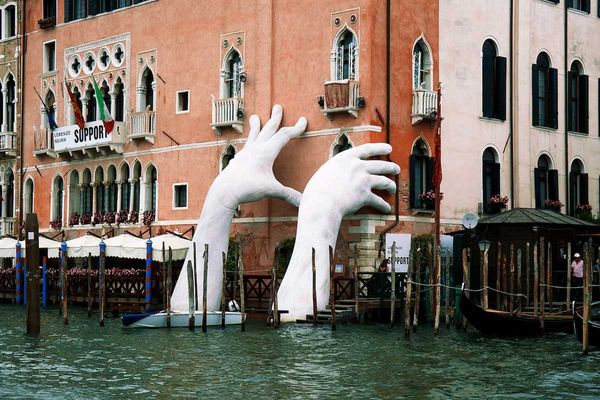 Gigantic hands rise from water to support the Ca' Sagredo Hotel, a statement of the impact of climate change and rising sea levels.