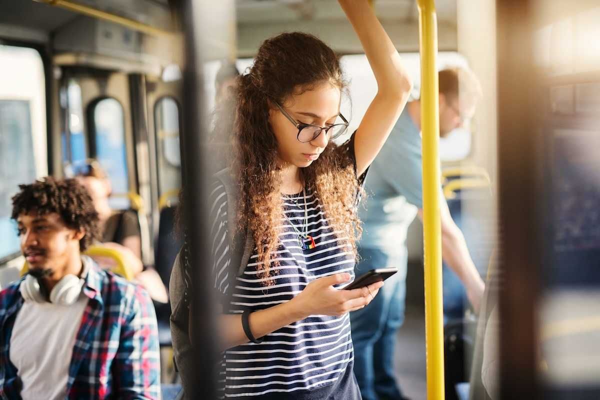 Girl riding bus while standing and checking cell phone