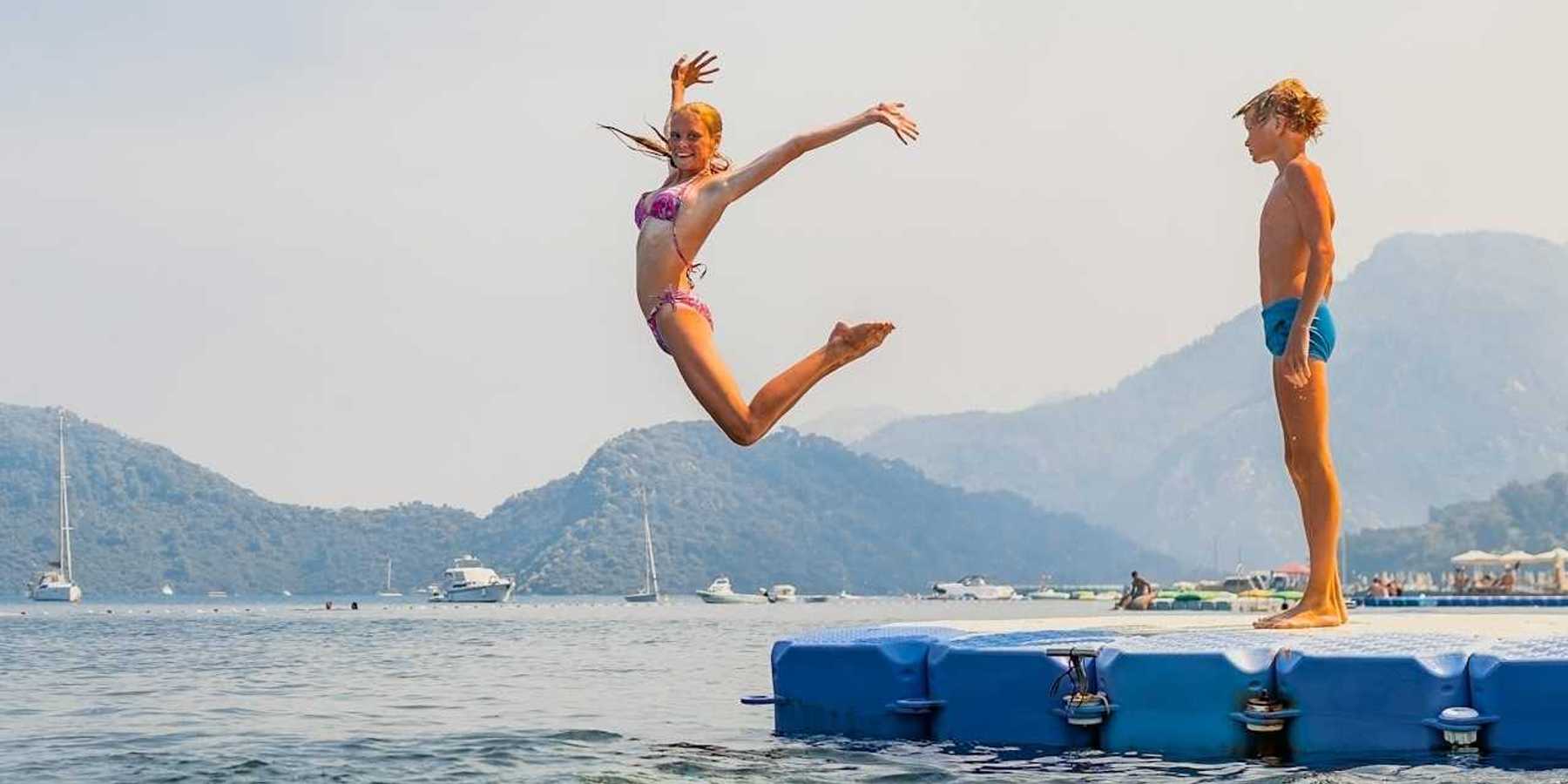 Girl striking a mid-air pose while jumping into water - boy stands and waits his turn