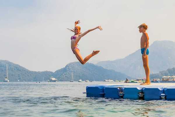 Girl striking a mid-air pose while jumping into water - boy stands and waits his turn