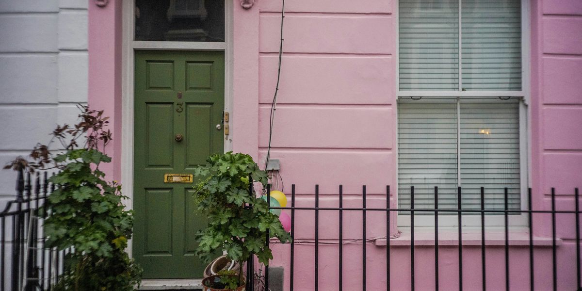 green leafed plants on the stoop next to a pink townhouse with a green door.