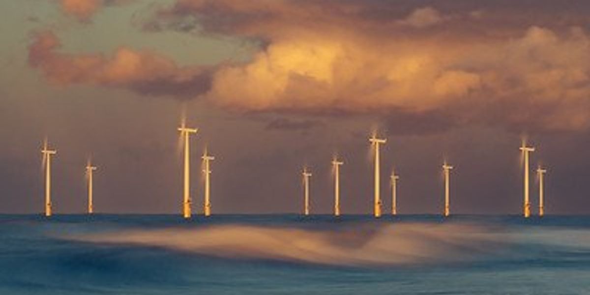 Group of offshore wind turbines bewteen clouds and waves.