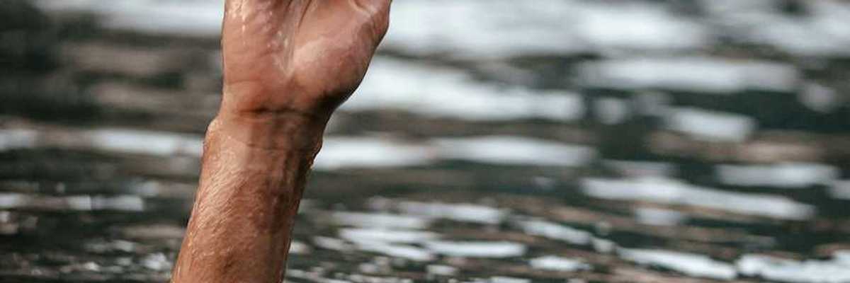 Hand and partially submerged forearm sticking out of floodwaters, one finger pointing up