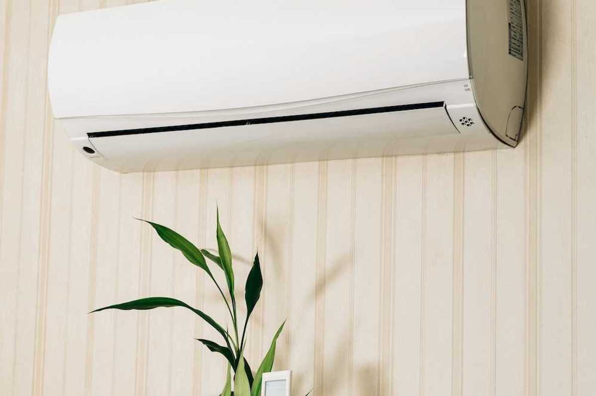 Hand holding a remote control directed at a wall-mounted mini-split heating unit