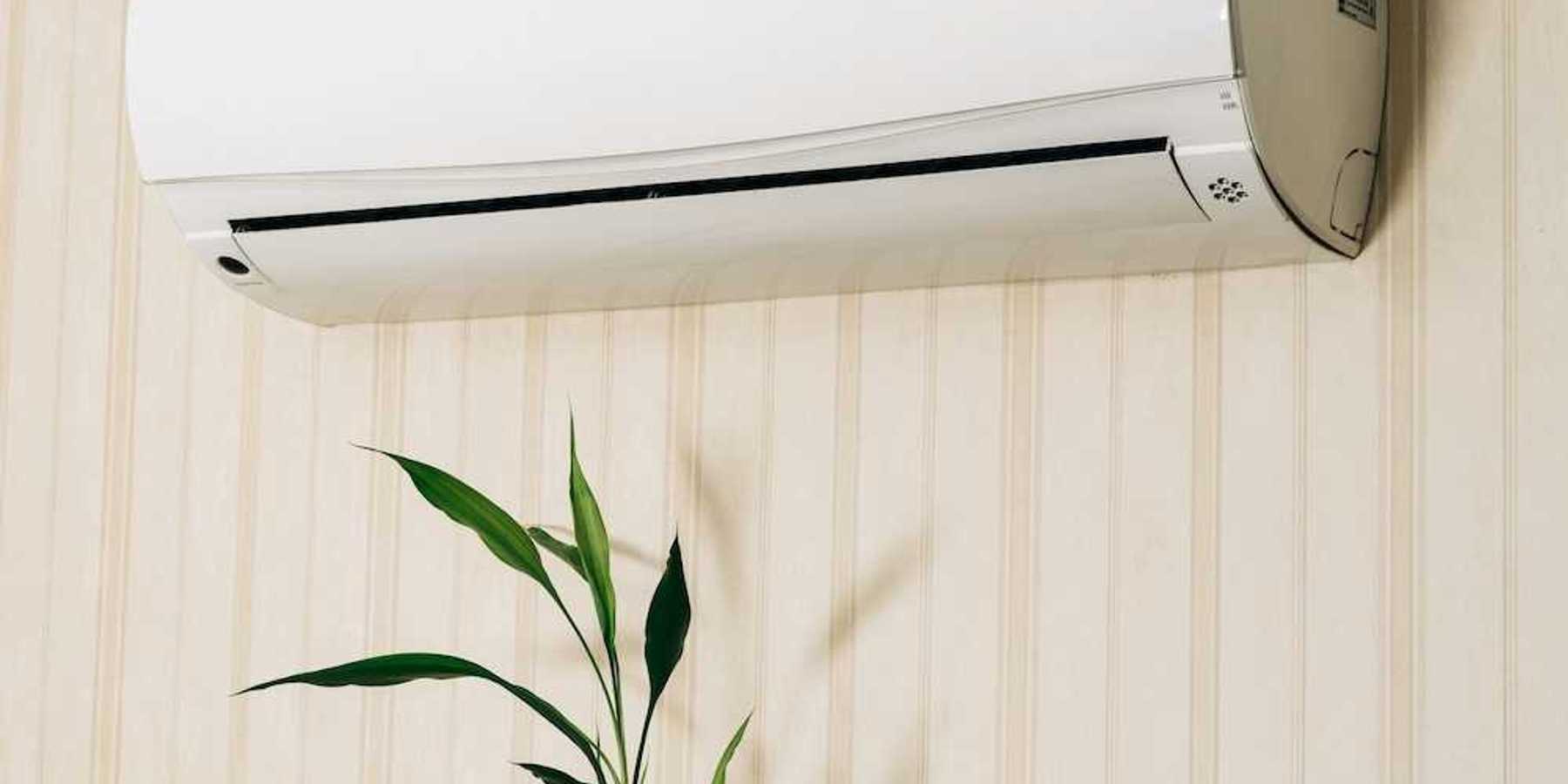 Hand holding a remote control directed at a wall-mounted mini-split heating unit