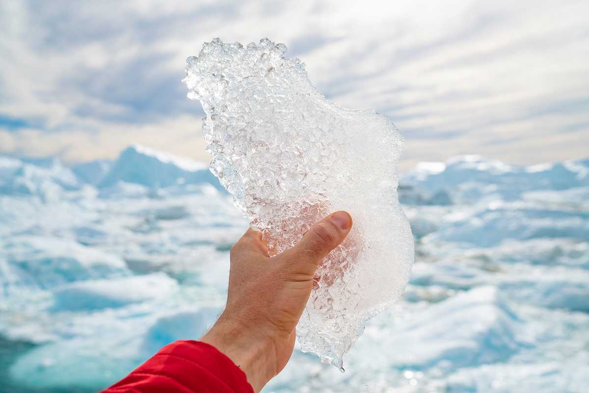 Hand holding melting ice by giant iceberg in Ilulissat icefjord on Greenland.
