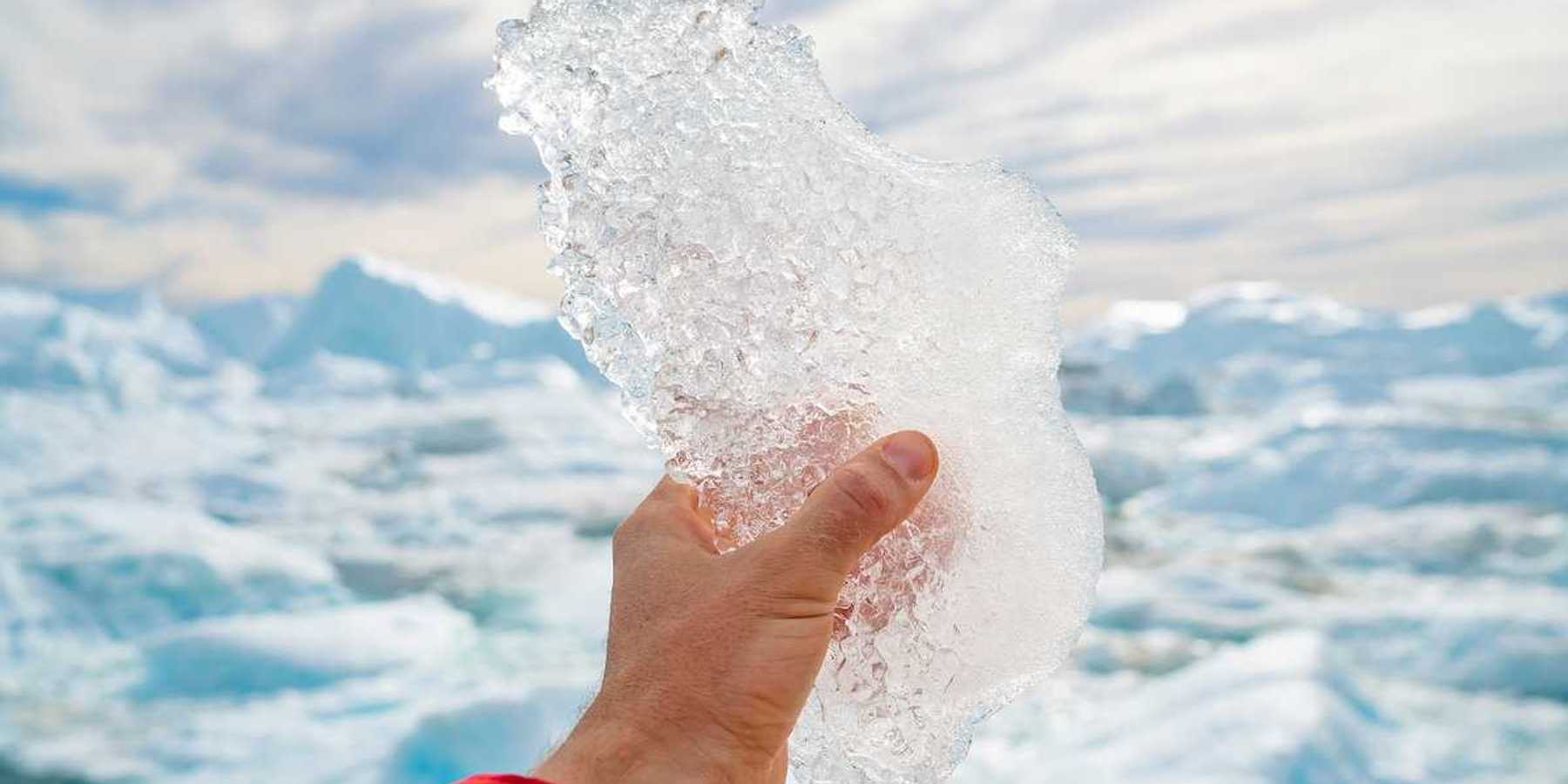 Hand holding melting ice by giant iceberg in Ilulissat icefjord on Greenland.