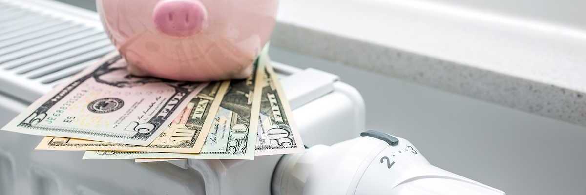 Heating thermostat on space heater with piggy bank and money indicating expensive heating costs