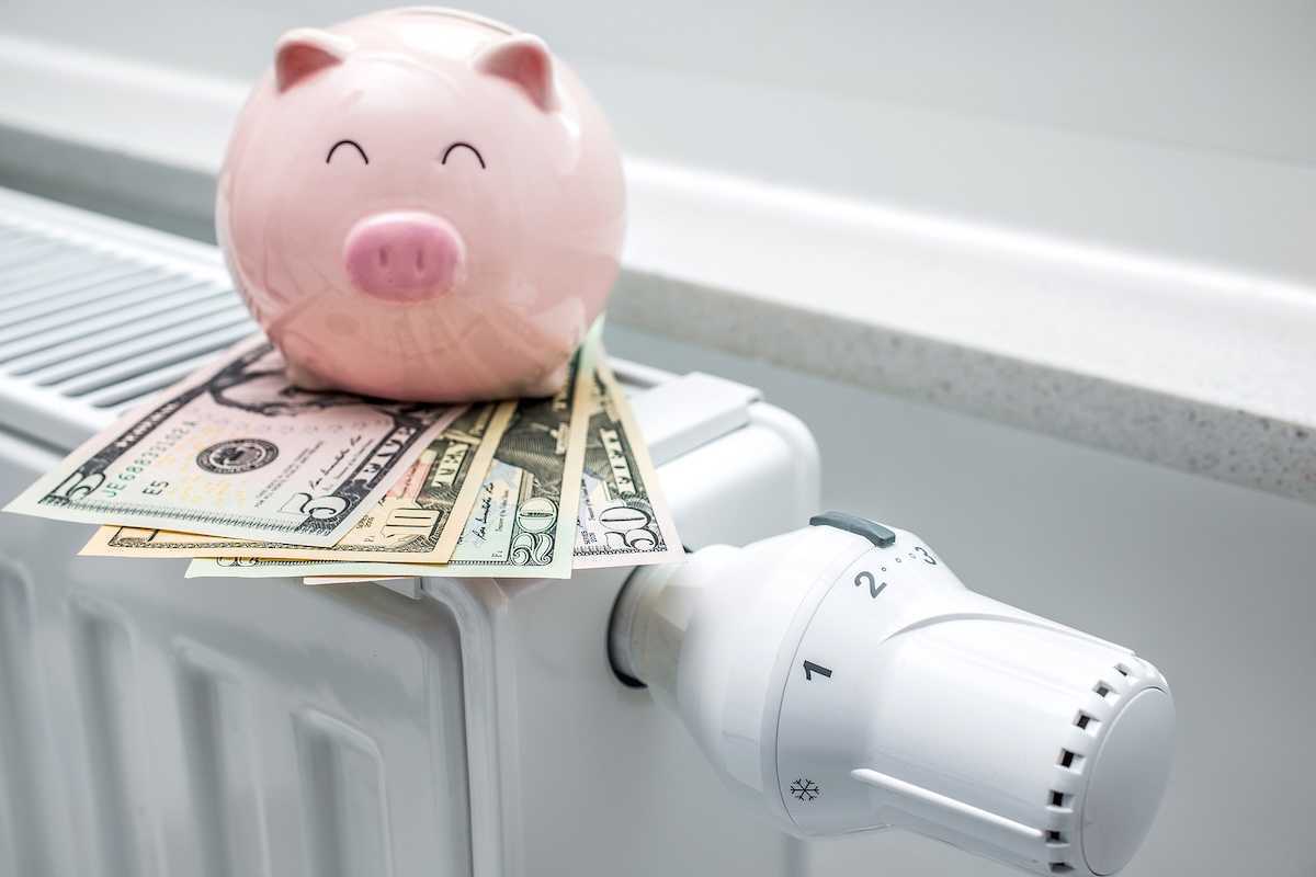 Heating thermostat on space heater with piggy bank and money indicating expensive heating costs