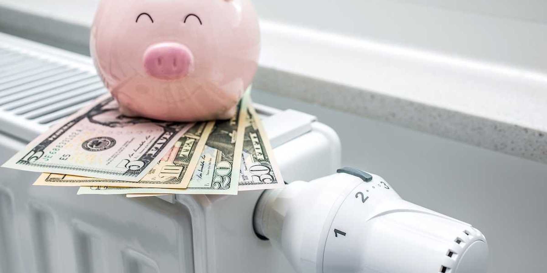 Heating thermostat on space heater with piggy bank and money indicating expensive heating costs
