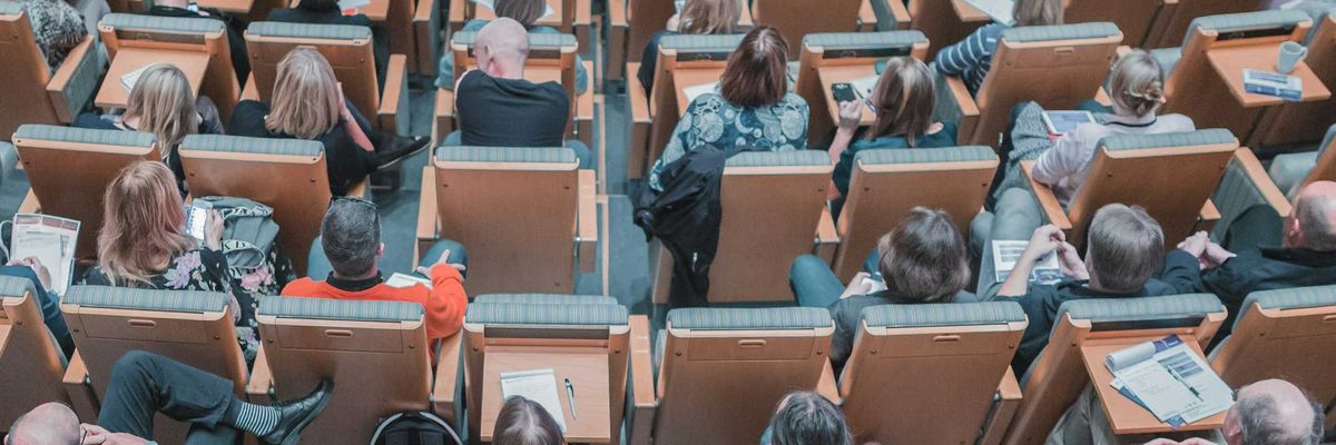 high-angle photography of group of people sitting at chairs in a conference auditorium.