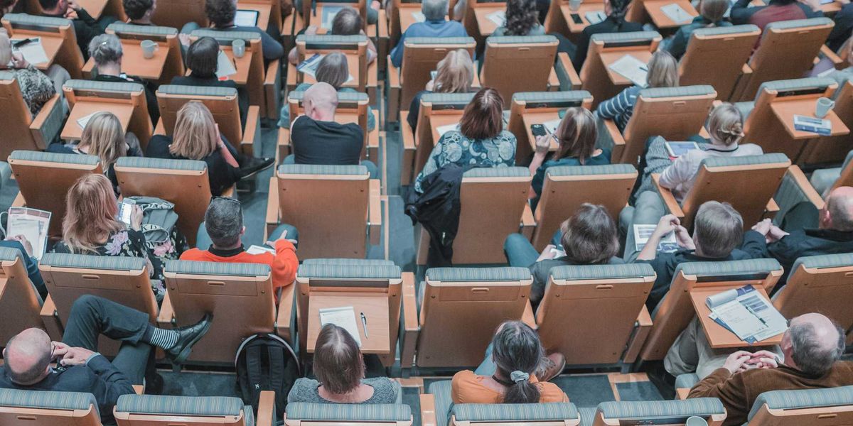 high-angle photography of group of people sitting at chairs in a conference auditorium.