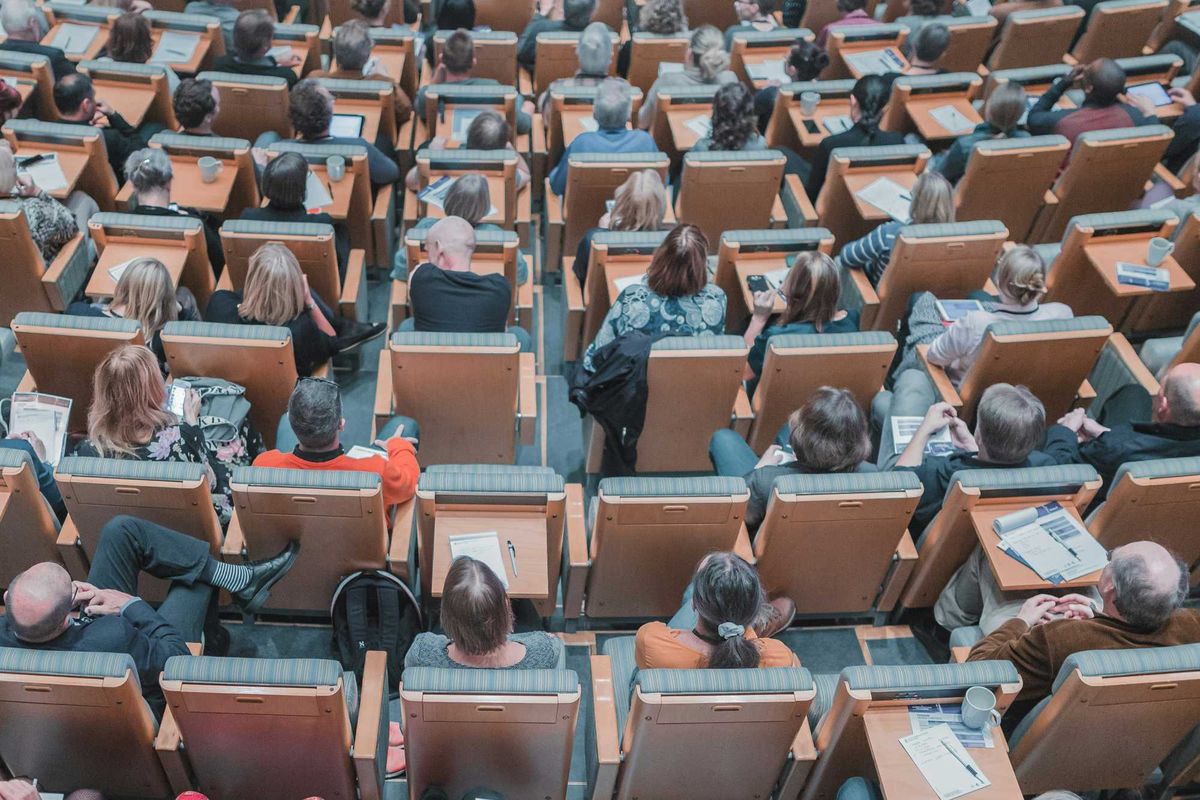 high-angle photography of group of people sitting at chairs in a conference auditorium.