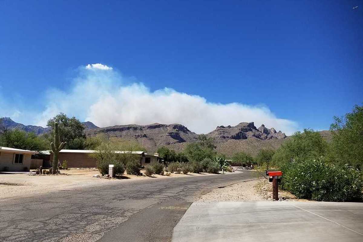 Homes in a dry landscape with wildfire smoke billowing in the background