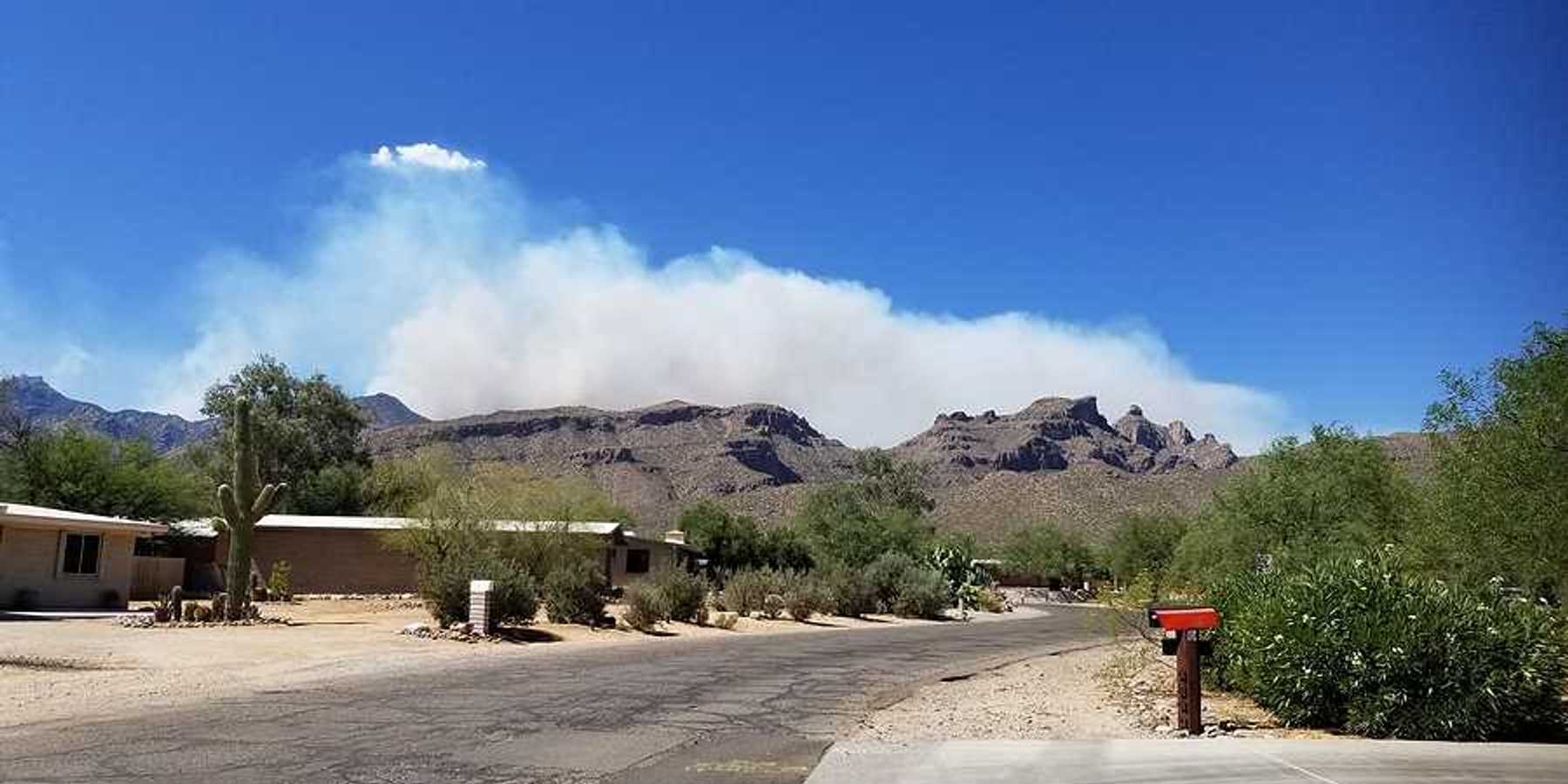 Homes in a dry landscape with wildfire smoke billowing in the background