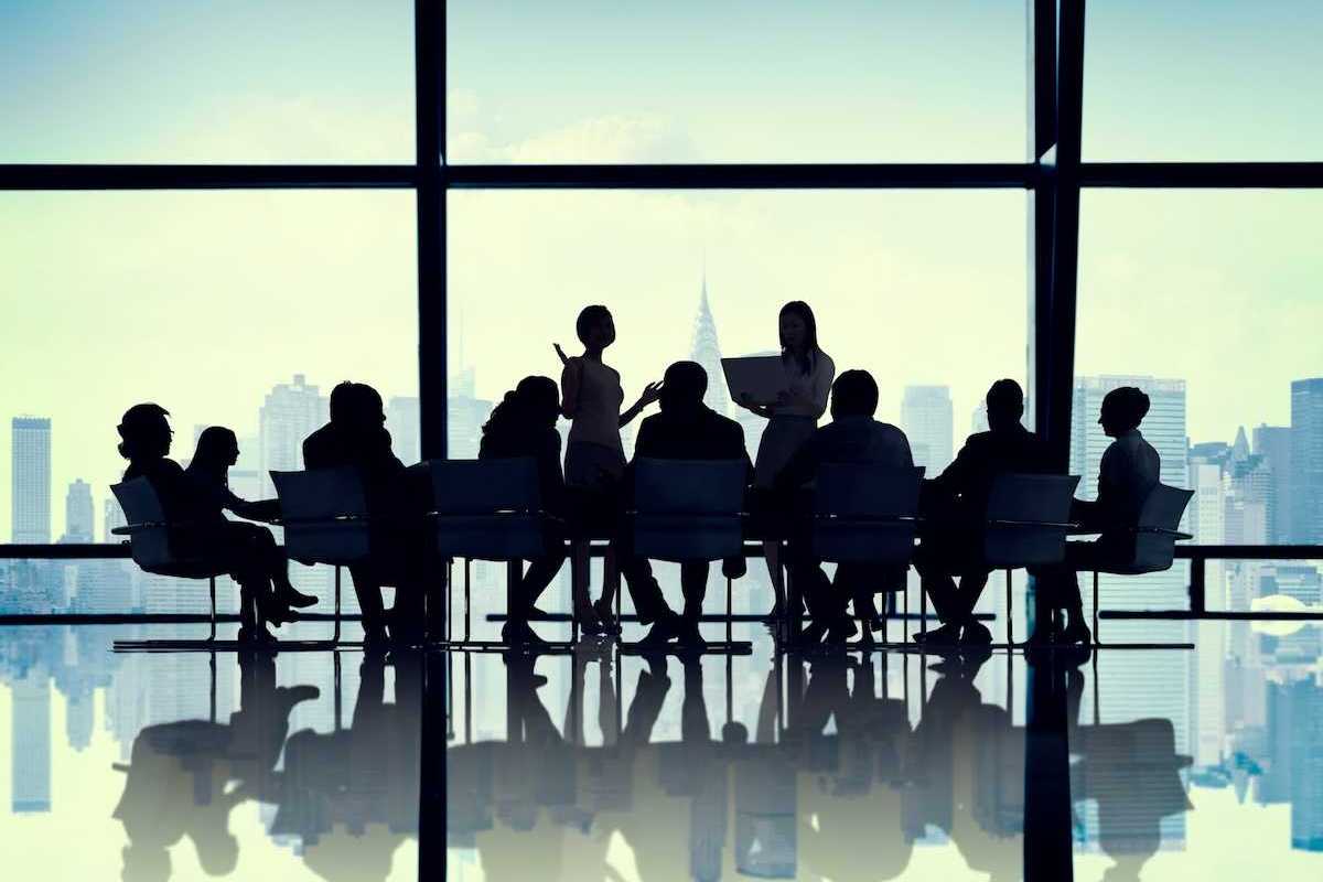 Illustration of silhouetted buisiness people gathered around a conference table against a cityscape background