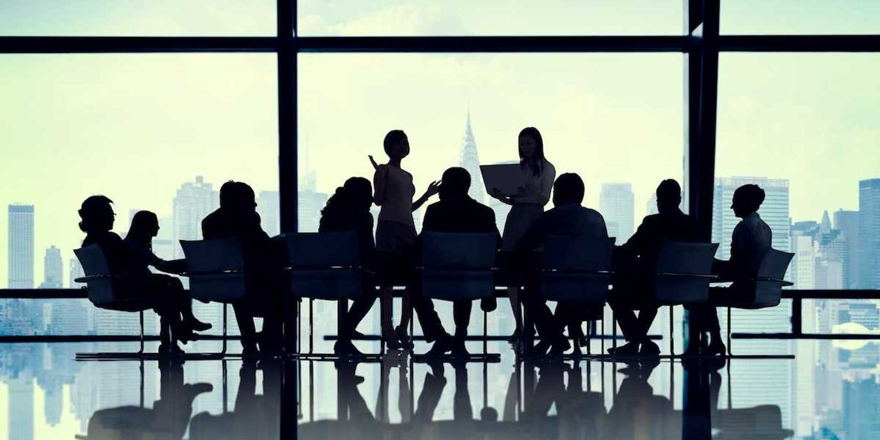 Illustration of silhouetted buisiness people gathered around a conference table against a cityscape background