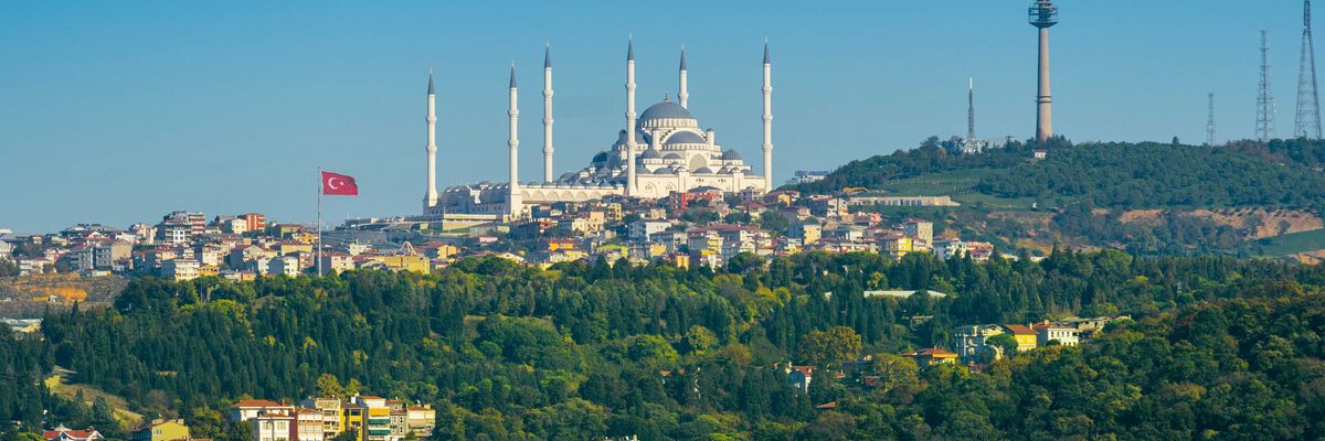 Image of a city in Turkey with ornate buildings on a hillside and a body of water in foreground.