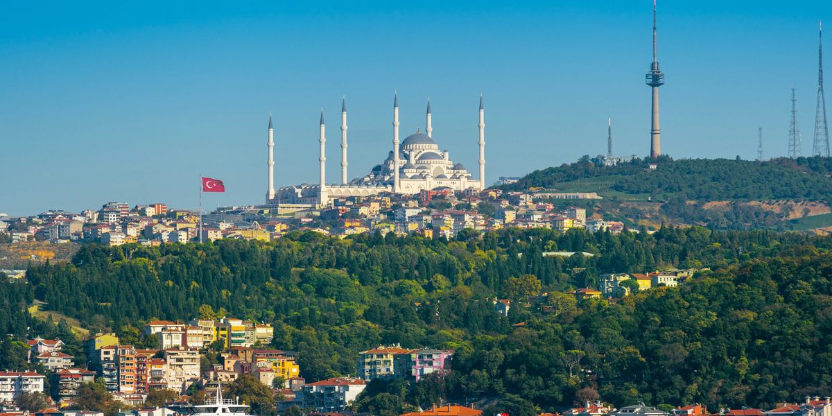 Image of a city in Turkey with ornate buildings on a hillside and a body of water in foreground.