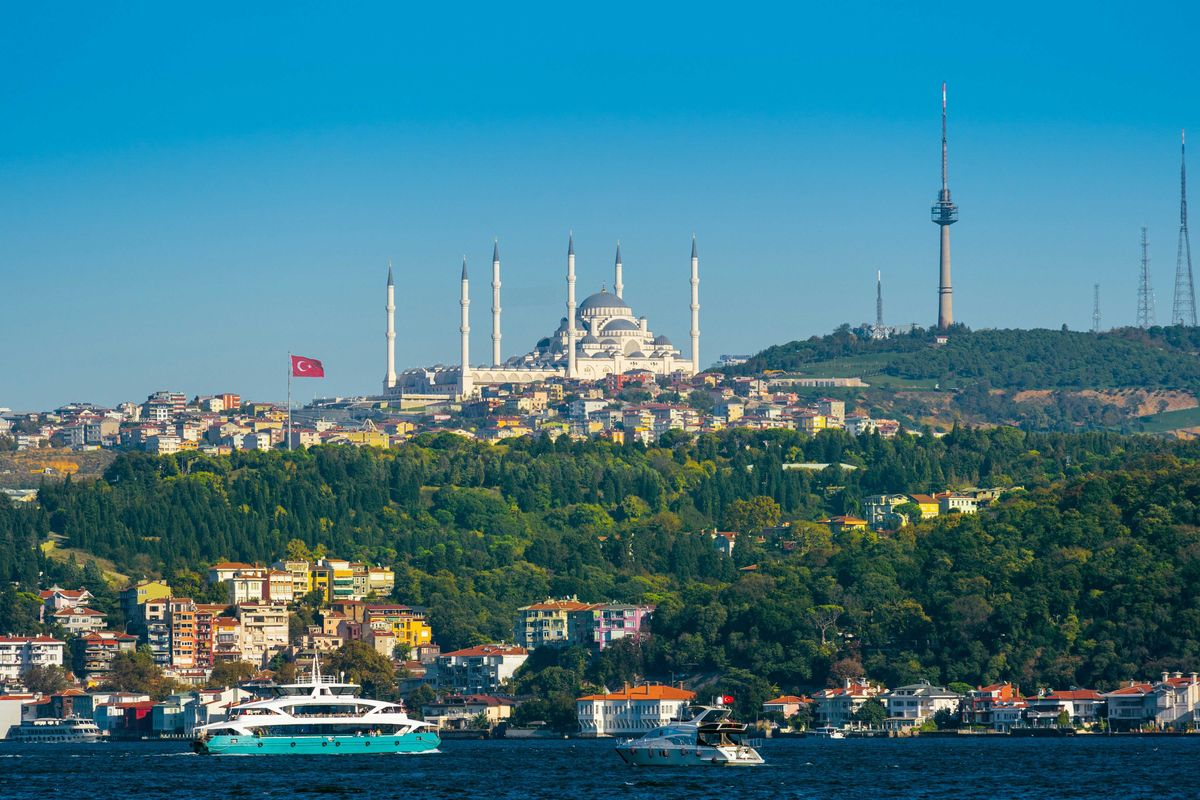 Image of a city in Turkey with ornate buildings on a hillside and a body of water in foreground.