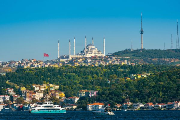 Image of a city in Turkey with ornate buildings on a hillside and a body of water in foreground.