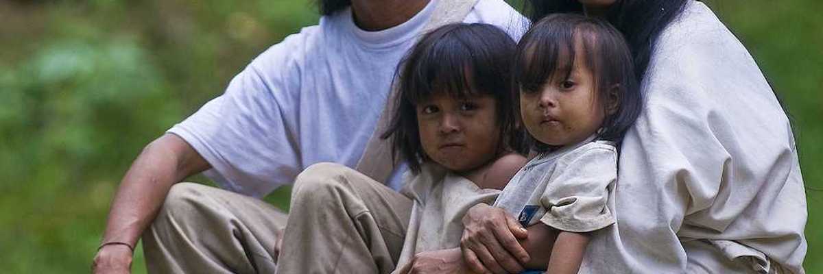 Indian family — man, woman, and two small girls — sit together at home in a village in "Tayrona" park Colombia