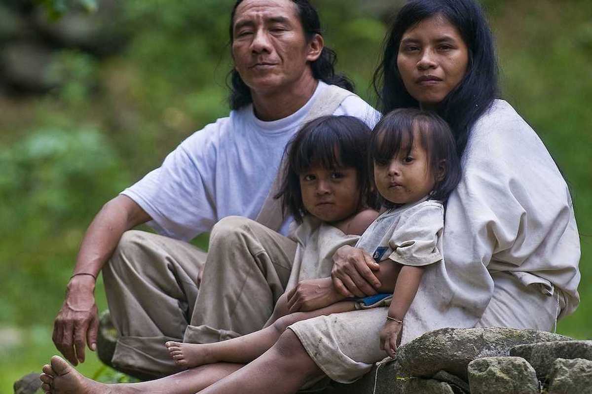 Indian family — man, woman, and two small girls — sit together at home in a village in "Tayrona" park Colombia