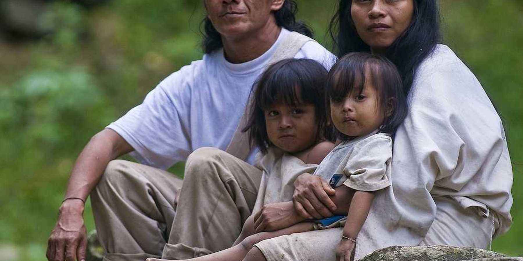 Indian family — man, woman, and two small girls — sit together at home in a village in "Tayrona" park Colombia