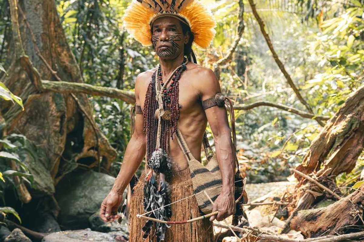 Indigenous Amazonian clad in traditional garb, standing in a rain forest