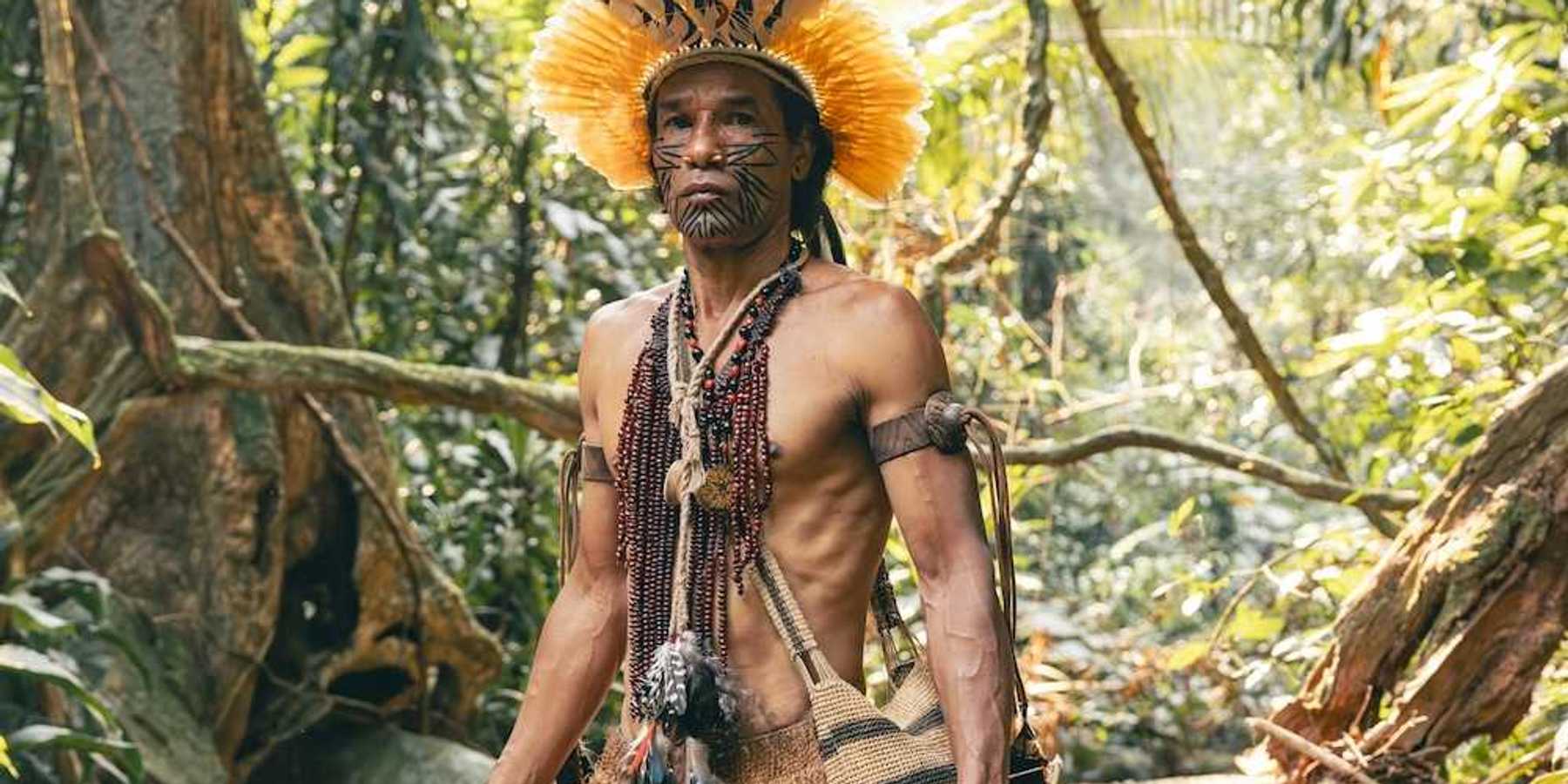 Indigenous Amazonian clothed in traditional dress, carrying traditional implements & weapons