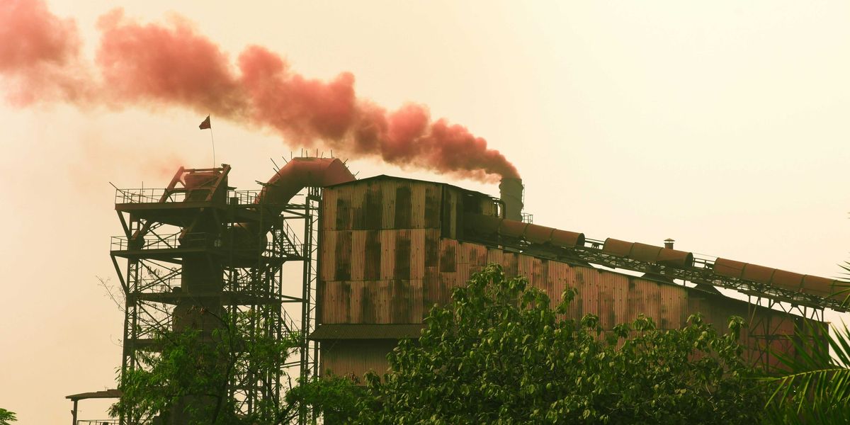 Industrial factory emitting red smoke against a hazy sky.
