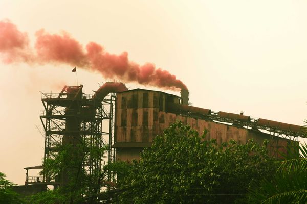 Industrial factory emitting red smoke against a hazy sky.
