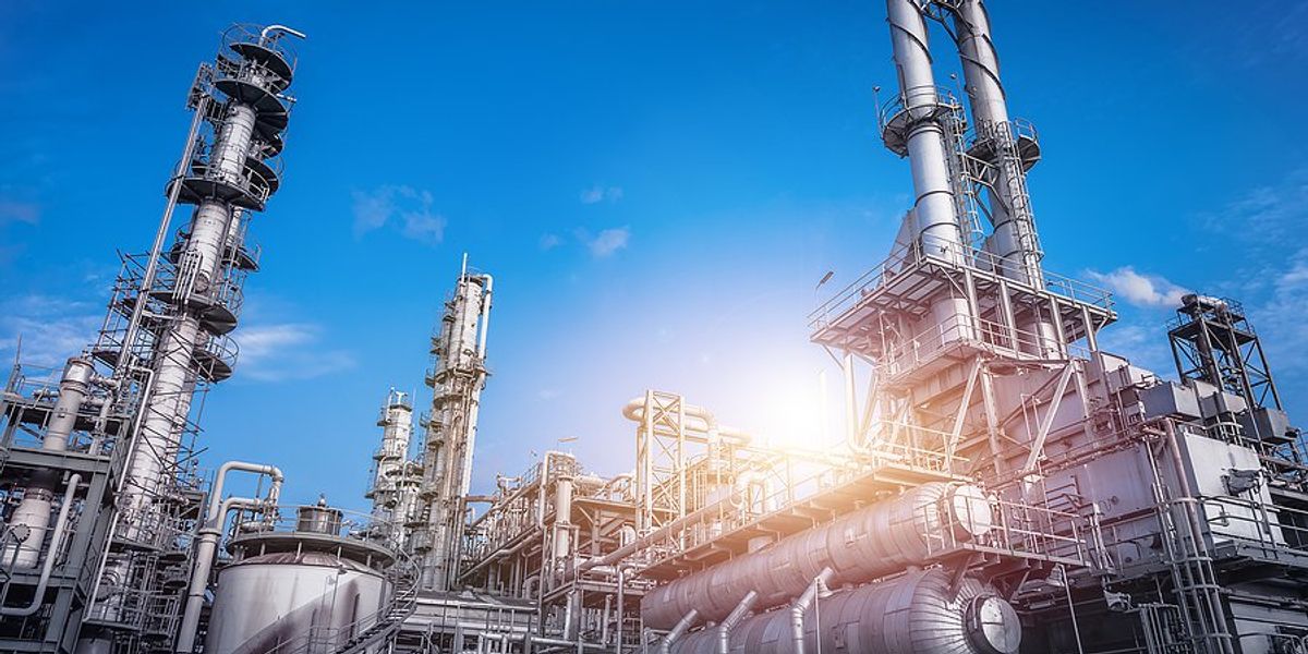 Industrial plant against backdrop of rising sun and blue sky.