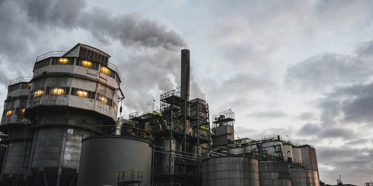 Industrial site with pipes and silver buildings and a cloudy gray sky in background.