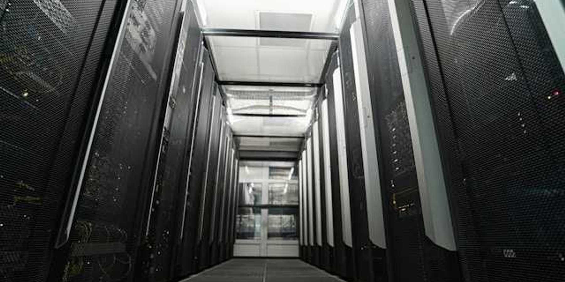 Inside of a data center with black computers on either side of a pathway to walk through
