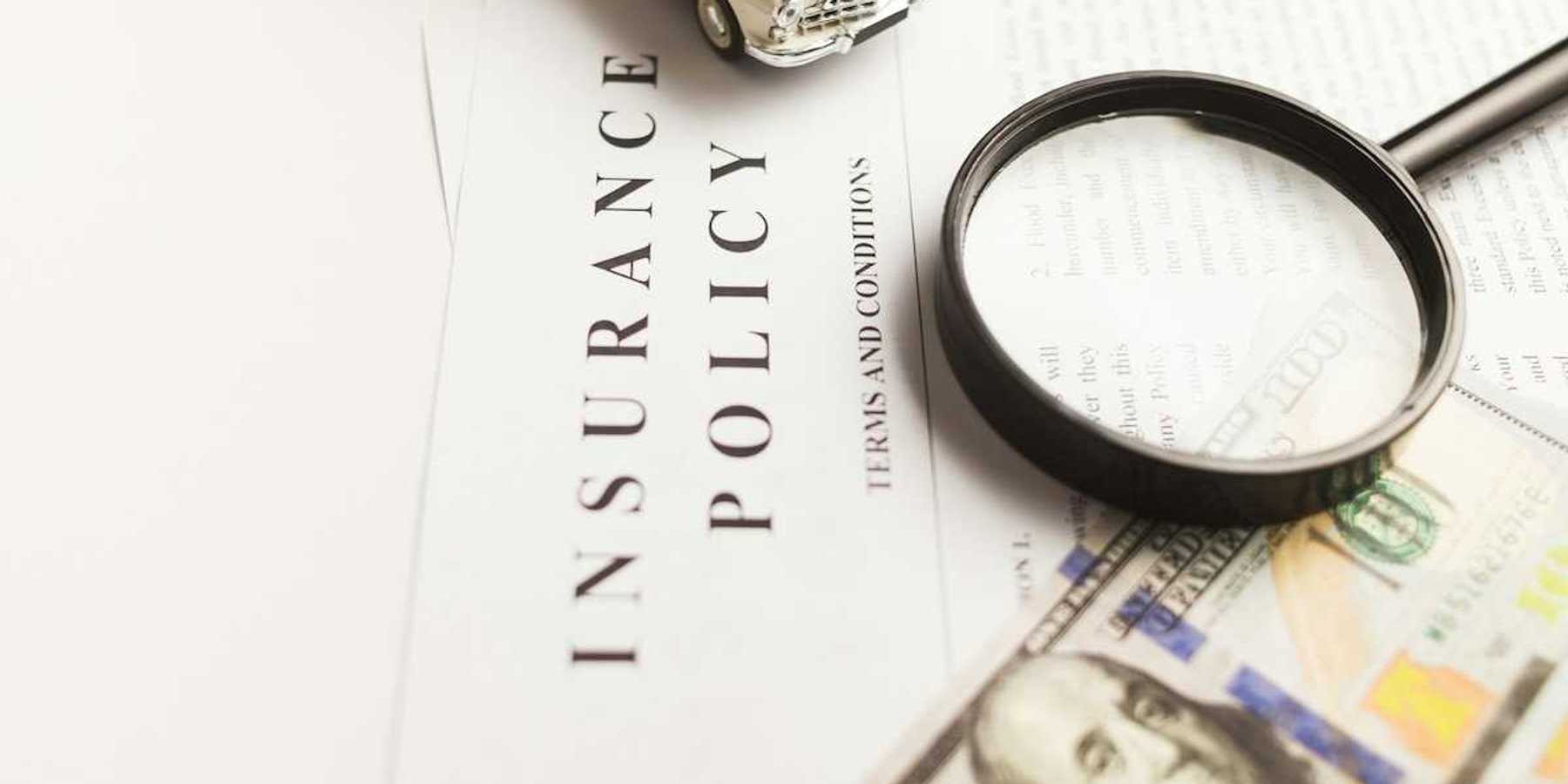 Insurance policy with magnifying glass, miniature auto, and hundred-dollar bill