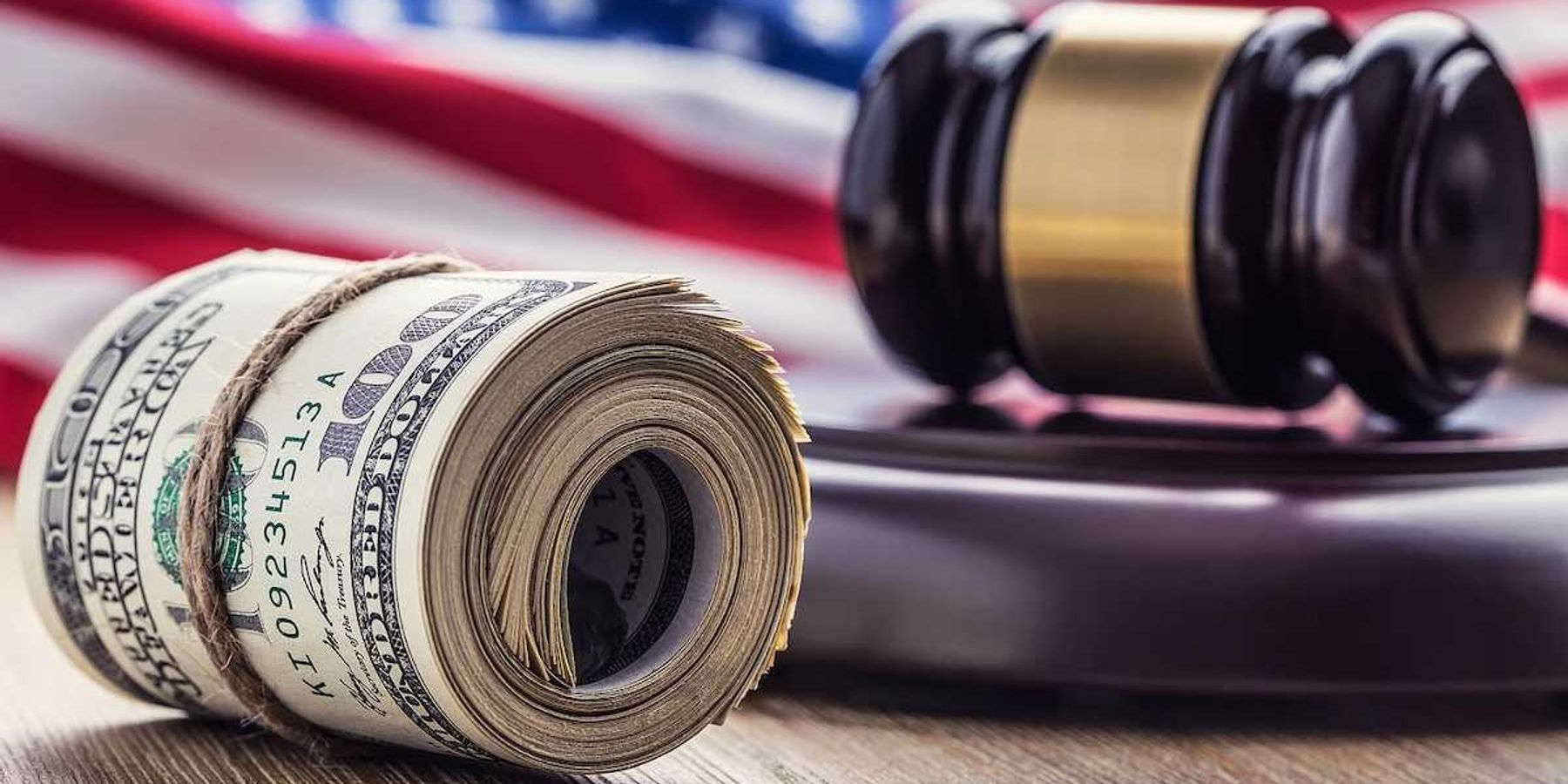 Judge's hammer gavel and rolled banknotes with USA flag in the background.