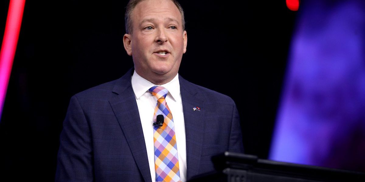 Lee Zeldin stands at a podium wearing a blue suit jacket and multi-colored checkered tie.