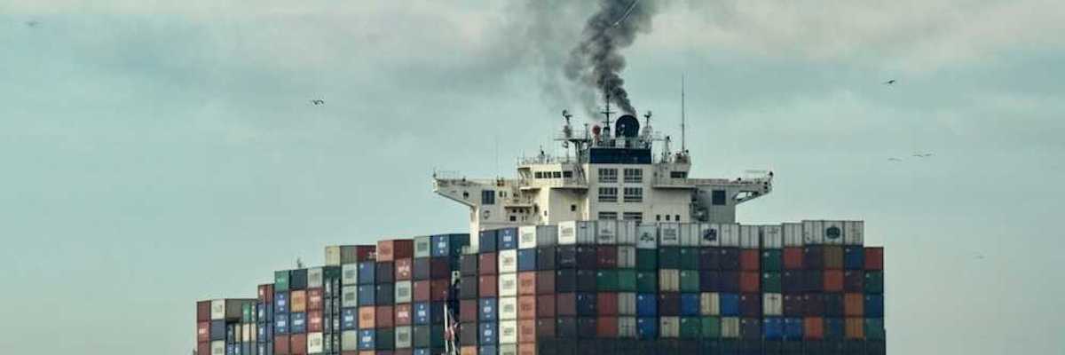 Loaded container ship on open sea belching black smoke