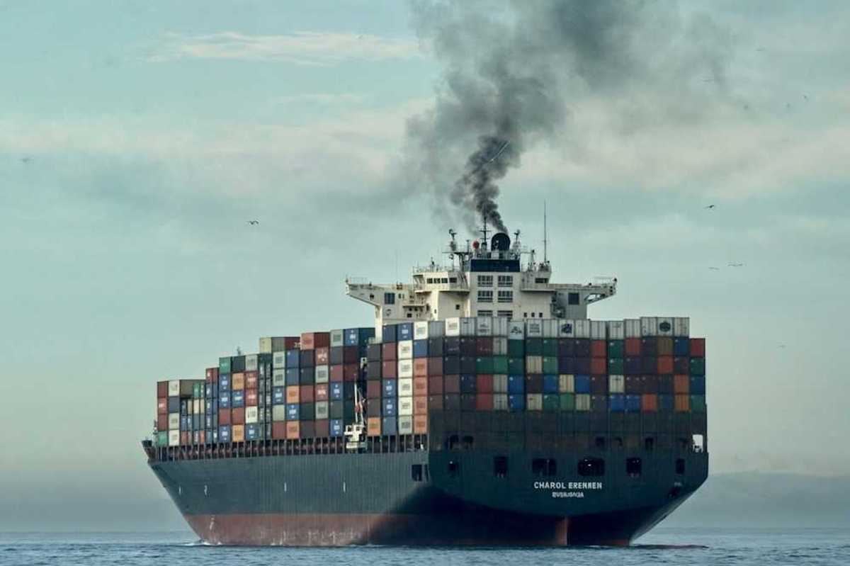 Loaded container ship on open sea belching black smoke
