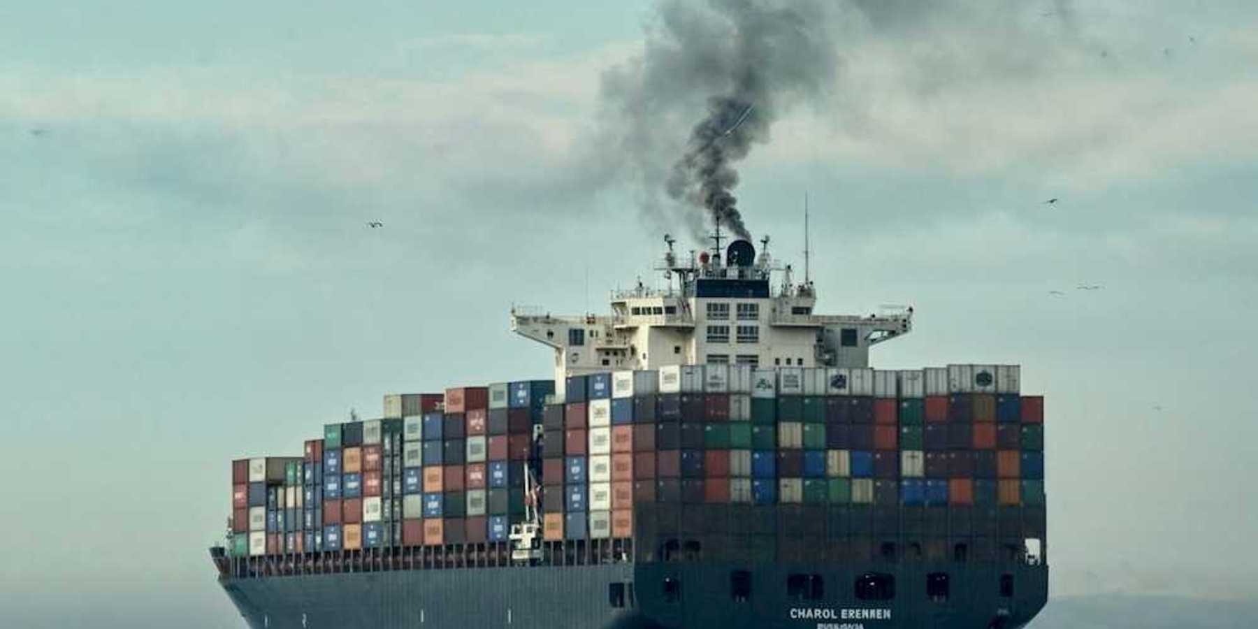 Loaded container ship on open sea belching black smoke