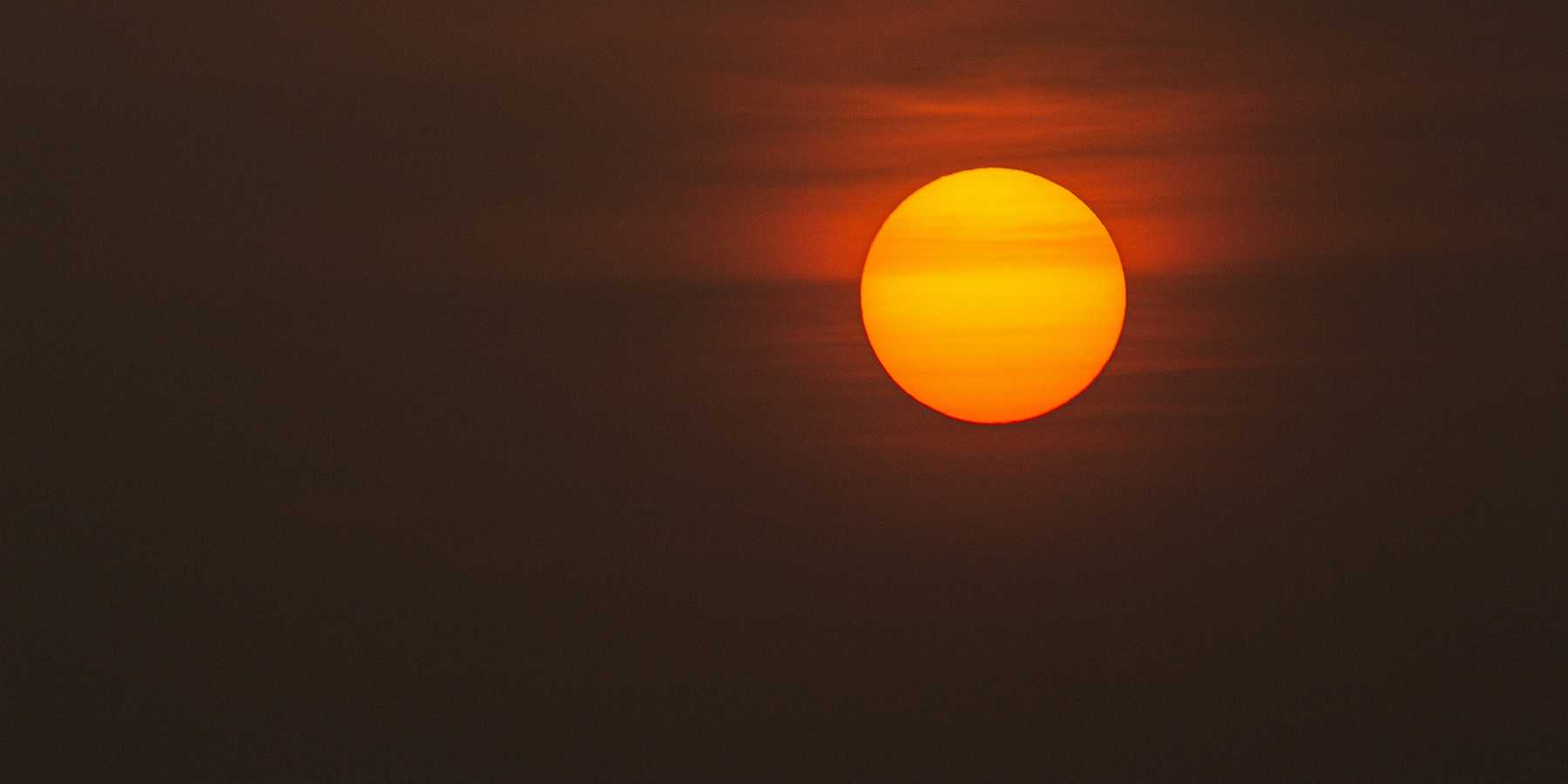 low-light photo of sun against a dark grey and orange sky.