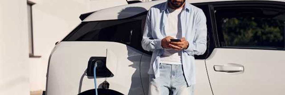 Man checking his phone while waiting for his electric vehicle to charge