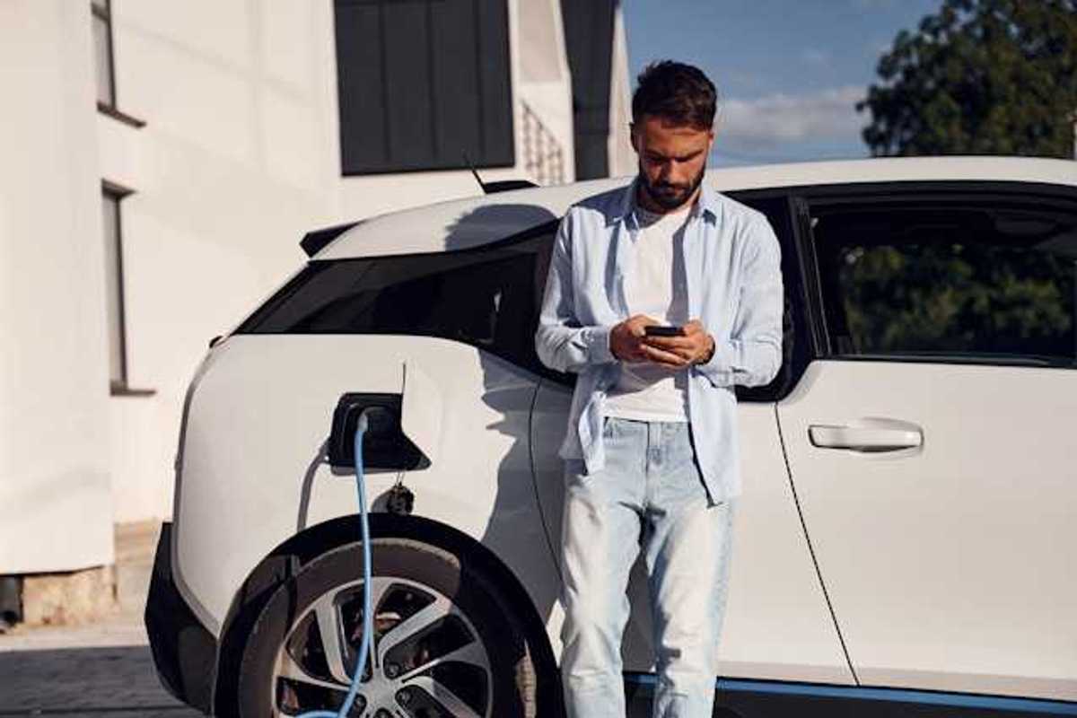 Man checking his phone while waiting for his electric vehicle to charge