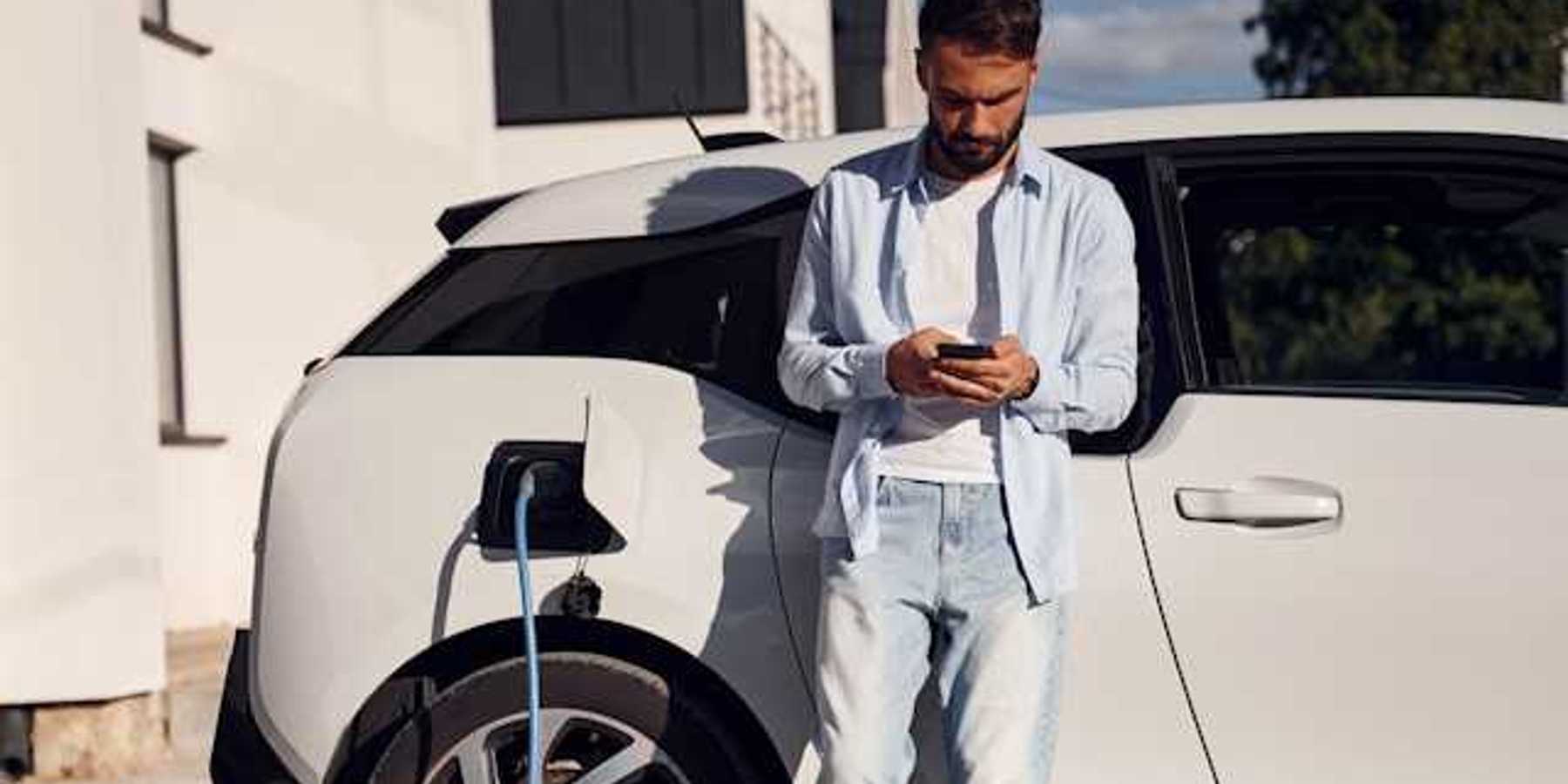 Man checking his phone while waiting for his electric vehicle to charge